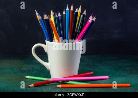 Seitenansicht eines Bündels Buntstifte in einer weißen Tasse auf dunklem Hintergrund Stockfoto