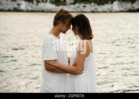 Romantisches kaukasisches Paar, das am Meer steht und sich in die Augen schaut und einander hält Stockfoto