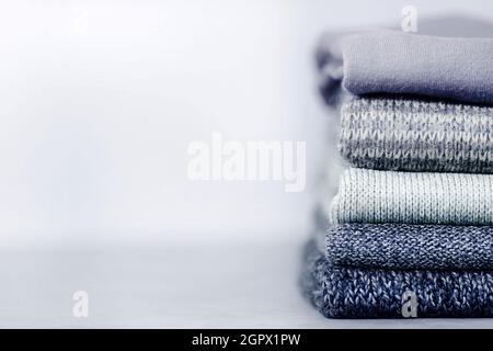 Stapel gestrickter Pullover und Pullover auf grauem, unscharfem Beton-Hintergrund. Speicherplatz kopieren Stockfoto