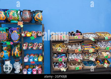 Ausstellung mexikanischer Handwerkskunst auf einem Regal an einer blauen Wand in einem Souvenirladen in Mexiko Stockfoto