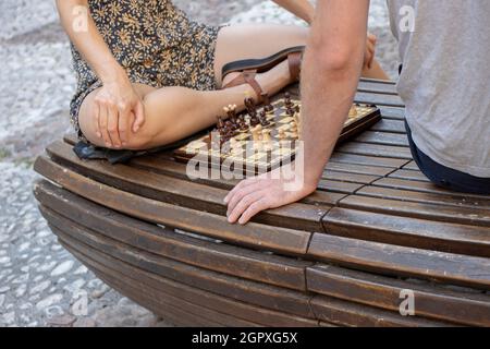 Junges Paar, das auf einer Parkbank in der Stadt Schach spielt Stockfoto