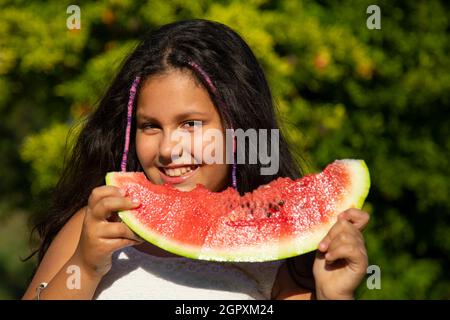 gypsy Mädchen mit langen schwarzen Haaren isst die große Scheibe Wassermelone Stockfoto