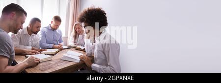 Gruppe von Jungen multiethnischen Menschen Lesen der Bibel über Holz- Schreibtisch Stockfoto