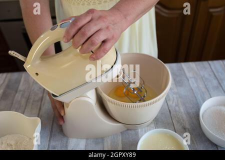 Schritt für Schritt der Prozess der Herstellung von Sauerrahm Pie Teig. Der Mixer schlägt die Eier in der Teigschale. Backkonzept. Stockfoto