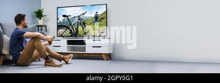 Mann, der im Wohnzimmer einen angeschlossenen Fernsehbildschirm sieht Stockfoto