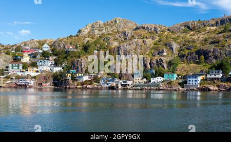 Der Hang des St. John's Harbour, an einem sonnigen Tag, unter blauem Himmel und weißen Wolken. Die bunten Holzhäuser sind entlang des Hügels verstreut Stockfoto