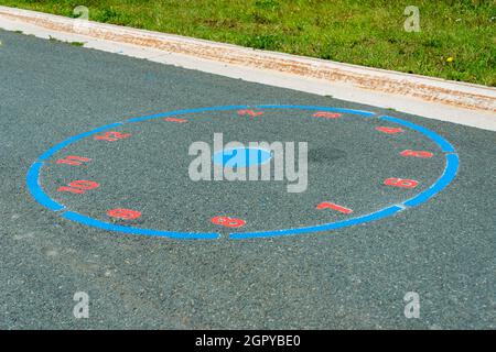 Auf dem Bürgersteig in einem Kinderpark sind farbenfrohe rote Zahlen gemalt. Das Schulübungsspiel ist eine rund um die Uhr mit einem blauen Punkt in der Mitte. Stockfoto