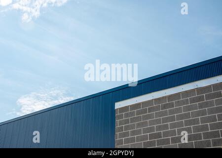 Die Außenwand eines Geschäftsgebäudes mit grauem Ziegelstein, hellgrauem Mörtel und silberfarbenem Blinken oder Faszien. Die Wand ist tiefblaues Blech Stockfoto