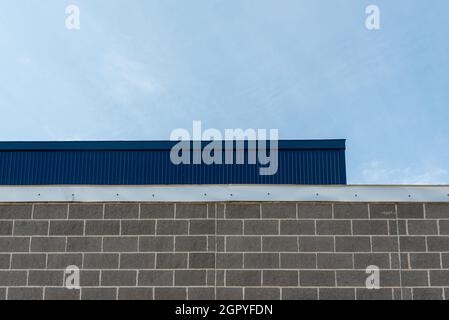 Die Außenwand eines Geschäftsgebäudes mit grauem Ziegelstein, hellgrauem Mörtel und silberfarbenem Blinken oder Faszien. Es gibt ein tiefblaues Blech. Stockfoto