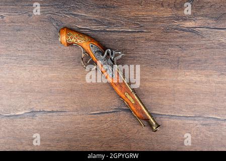 Nachbildung einer alten Pistole mit Bronzeeinlage auf einem Holzhintergrund. Speicherplatz kopieren. Stockfoto