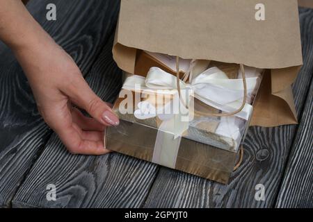 Eine Frau legt selbstgemachte Marshallows in eine Bastelkiste in eine Papiertüte. Marshallow in einem Waffelkegel. Hergestellt in der Form einer Rose. Nahaufnahme. Stockfoto