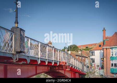 Niedrige Ansicht einer Eisenbrücke. Die Leute gehen durch und es gibt ein öffentliches Haus auf der anderen Seite. Ein Himmel mit einer leichten Wolke ist oben. Stockfoto