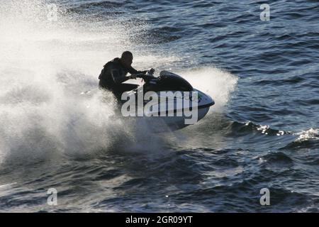 Firth of Clyde Scotland, Großbritannien 2005. Ein Jet-Ski surrt um die Caledonian MacBrayne Ferry auf der Caledonian Isle. Während es ein spektakuläres Spektakel war, wurde iit als hochgefährlich mit der Welle, die durch die Bugwelle des Schiffes verursacht wurde, eingestuft. Es ist ein kleines Jet-Propelled Fahrzeug, das über die Wasseroberfläche abrutscht und in der Regel wie ein Motorrad gefahren wird. Stockfoto