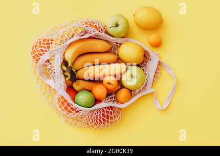 Baumwolltasche aus Mesh mit frischen bunten Früchten auf gelbem Hintergrund, Draufsicht. Zero Waste Konzept Stockfoto