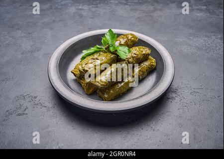 Köstliche gefüllte Traubenblätter Dolma mit Petersilie in schwarzem Teller auf dunklem Holz Hintergrund. Stockfoto