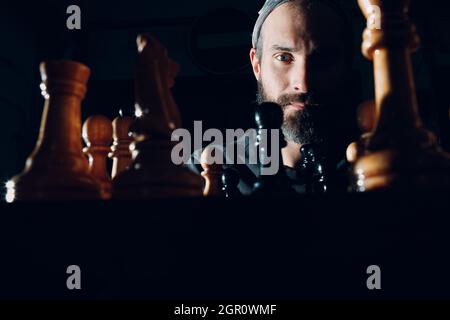 Junger, hübscher Mann, der im Dunkeln Schach spielt und seitlich beleuchtet ist. Stockfoto