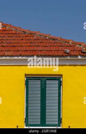 Hell gestrichenes gelbes griechisches Haus mit grünen Holzfensterläden und Terrakotta-Dachziegeln auf der griechischen Insel Zante zakynthos. Gelb gestrichen Stockfoto