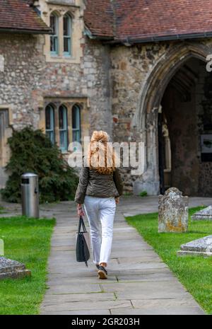 Frau mittleren Alters mit langen roten Haaren, die allein durch einen Kirchhof in der chichester Kathedrale nach Hause geht. dame, die allein mit einer Tasche geht. Einsame Dame. Stockfoto