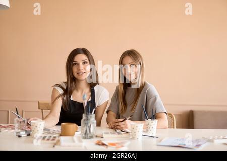 Vorderansicht von vier schönen kaukasischen Weibchen in der Kunstwerkstatt. Ein junger Lehrer lehrt Zeichnen Stockfoto