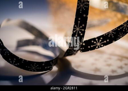 Verdrehtes schwarzes Zierband mit Punkten in Form von Stern, Blume oder Schneeflocke auf dem Hintergrund mit Schatten mit Sternen aus verschwommenem goldenem Stoff. Stockfoto