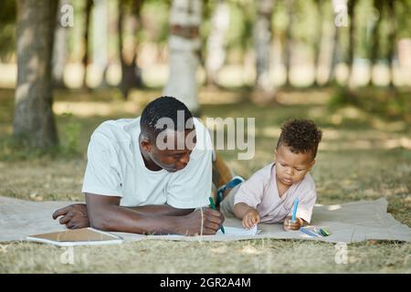 Porträt eines jungen afroamerikanischen Vaters, der mit einem niedlichen Sohn im Park spielt, während er auf Gras liegt und Platz kopiert Stockfoto