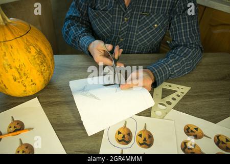 Jack O'Lantern zu Hause machen. Jack O'Lantern Thread-Vorlage erstellen Prozess. Der Mann bereitet den Kürbis zum Schnitzen vor. Stockfoto