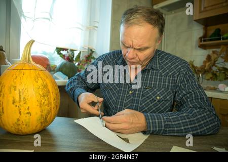 Jack O'Lantern zu Hause machen. Jack O'Lantern Thread-Vorlage erstellen Prozess. Der Mann bereitet den Kürbis zum Schnitzen vor. Stockfoto