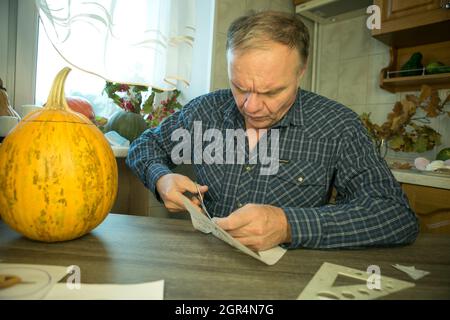 Jack O'Lantern zu Hause machen. Jack O'Lantern Thread-Vorlage erstellen Prozess. Der Mann bereitet den Kürbis zum Schnitzen vor. Stockfoto