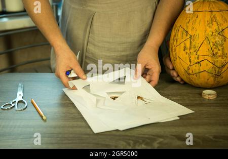 Halloween. Jack O'Lantern zu Hause machen. Jack O'Lantern Thread-Vorlage erstellen Prozess. Eine Frau bereitet den Kürbis zum Schnitzen vor. Stockfoto