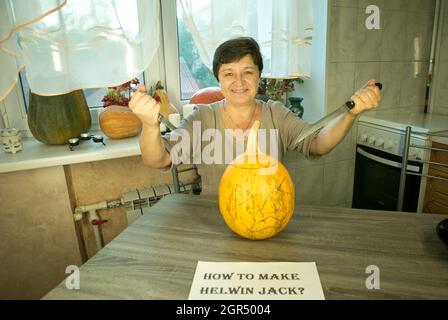 Jack O'Lantern zu Hause machen. Jack O'Lantern Thread-Vorlage erstellen Prozess. Eine Frau bereitet den Kürbis zum Schnitzen vor. Die Frau ist glücklich mit dem Stockfoto