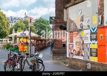 Berlin, Deutschland - August 27 2017; altes schmutzige Gebäude an der Ecke mit Rechnungen an der Wand, Fahrrädern auf dem Bürgersteig und einem Café-Tisch im Freien unter Sonnenschutz Stockfoto