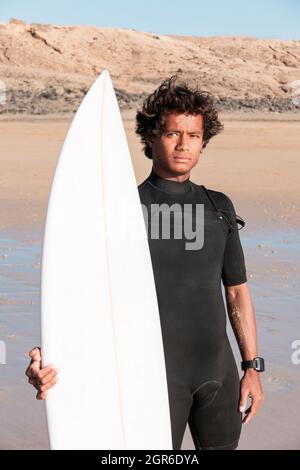 Das junge madagassische Surferportrait mit seinem Surfbrett, das am Strand steht Stockfoto