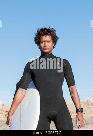 Junge afrikanische madagassische sportliche Surferportrait mit Surfbrett in kurzem schwarzen Neoprenanzug Stockfoto