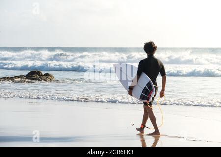 Nicht erkennbarer junger Surfer mit Shortboard, der am Strand entlang läuft und die Wellen beobachtet Stockfoto