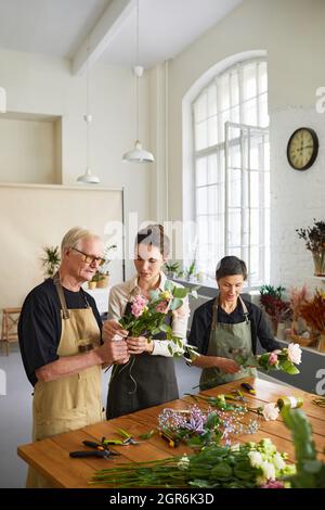 Vertikales Porträt einer jungen Frau Floristin, die reifes Paar unterrichtet und Blumenkompositionen in der Werkstatt arrangiert Stockfoto