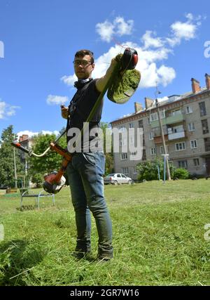 Kovrov, Russland. 28. Juni 2017. Im Innenhof des fünfstöckigen Wohnhauses mäht ein junger Mann das Gras mit einem benzinbetriebenen Unkrauttrimmer Stockfoto