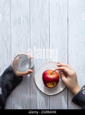 Minimaler Gesunder Snack-Konzept. Die Hände des Kindes halten einen Apfel und Ein Glas Wasser.