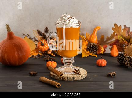 Kürbis-Latte in einem Glas-Becher mit Zimt, Muskatnuss und Schlagsahne würzen. Stockfoto
