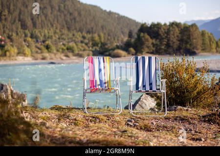 Klappstühle am Ufer eines Bergflusses an einem schönen, warmen Tag. Ein ruhiger und ruhiger Ort zum Entspannen und Nachdenken. Ausrüstung und die Erholung des Touristen. Stockfoto