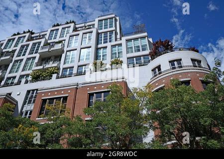 Apartmentgebäude, umgeben von Bäumen, mit Pflanzen auf Balkonen und Dach, was gut für die Umwelt ist Stockfoto