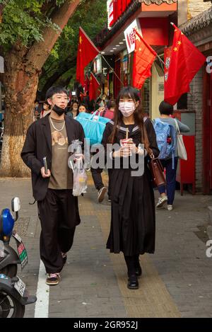 Peking, China. September 2021. Passanten gehen vor dem Nationalfeiertag und der Goldenen Woche in der Innenstadt von Peking, China, den Bürgersteig neben chinesischen Flaggen hinunter am 30/09/2021 von Wiktor Dabkowski Credit: dpa/Alamy Live News Stockfoto