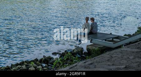 HERNE, DEUTSCHLAND - 31. Aug 2021: Ein liebevolles Paar, das sich entspannt vor dem Rhein-Herne-Kanal in Herne, Deutschland, sitzt Stockfoto