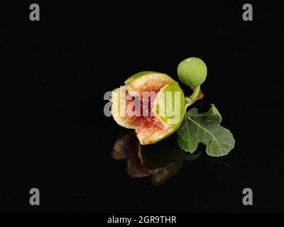 Reife grüne Feigenfrucht mit Blatt isoliert auf dunklem Hintergrund Stockfoto