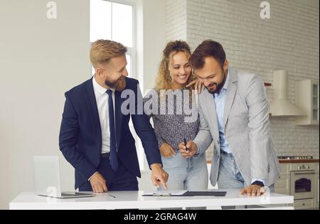 Glückliches junges Paar, das Haus kauft oder vermietet, mit dem makler zusammentreffen und Vertrag unterzeichnet Stockfoto