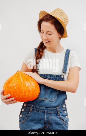 Frau im Overall hält einen großen Kürbis, der im Herbst geerntet wurde. Stockfoto