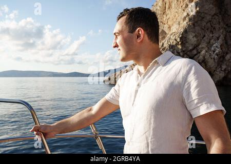 Junger Mann im weißen Hemd, der auf der Nasenyacht im Meer steht Stockfoto