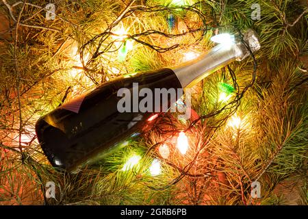Eine Flasche grünen Champagner, umhüllt von einer glühenden Girlande wie ein Weihnachtsbaum. Neues Jahr Konzept auf natürlichem Hintergrund. Copy Platz für Flasche Design Stockfoto