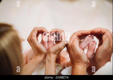 Die Beine des Neugeborenen werden in den Händen der Mutter und des Vaters in Form eines Herzens gehalten, die Füße der Kinder in den Händen der Eltern. Stockfoto