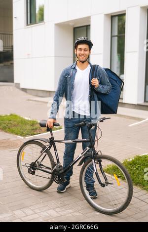 Hübscher junger Mann mit Schutzhelm, der in der Nähe des Fahrrads auf der Stadtstraße steht und die Kamera anschaut. Stockfoto