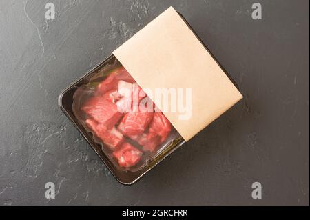 Portionierte Stücke von frischem Fleisch in Vakuumverpackung auf schwarzem Hintergrund. Draufsicht. Logo-Layout-Design. Das Konzept des schnellen Kochens Stockfoto